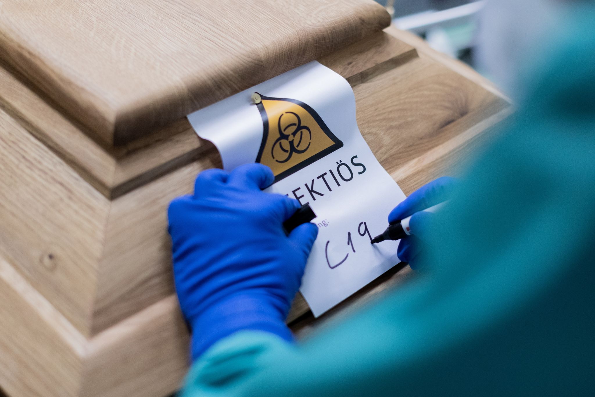 Ein Bestattungsunternehmer schreibt «C19» auf ein Schild mit dem Hinweis «Infektiös» auf einen Sarg mit einem Verstorbenen, der an dem Coronavirus gestorben ist. (© Rolf Vennenbernd/dpa)