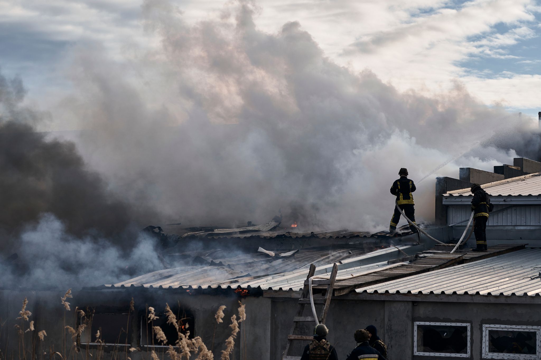 Feuerwehrleute des staatlichen ukrainischen Katastrophenschutzes löschen ein Feuer, das nach Beschuss eines Industriegebiets in Cherson ausgebrochen ist. (© Libkos/AP/dpa)